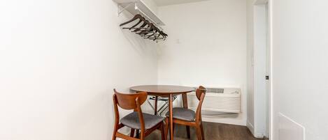 Un pequeño comedor con una mesa redonda y cuatro sillas de madera, una pared blanca y un equipo de aire acondicionado empotrado.