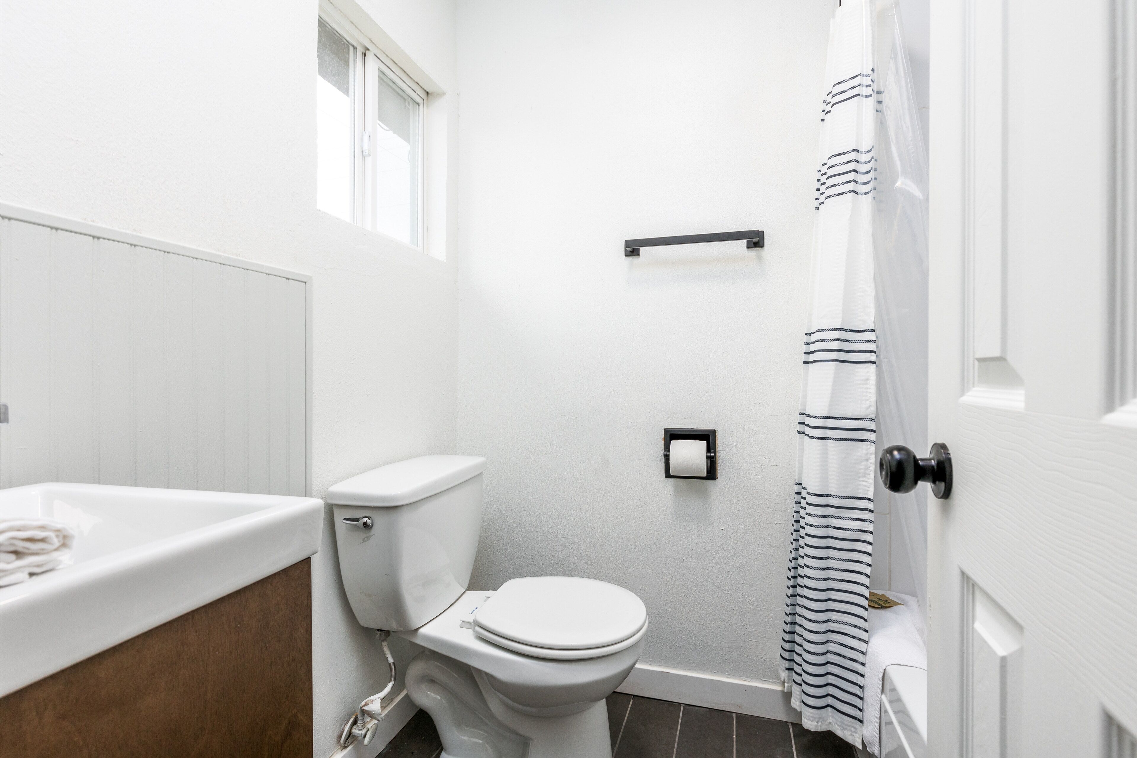 A bathroom with a white toilet, a sink, a shower curtain, and a towel rack.