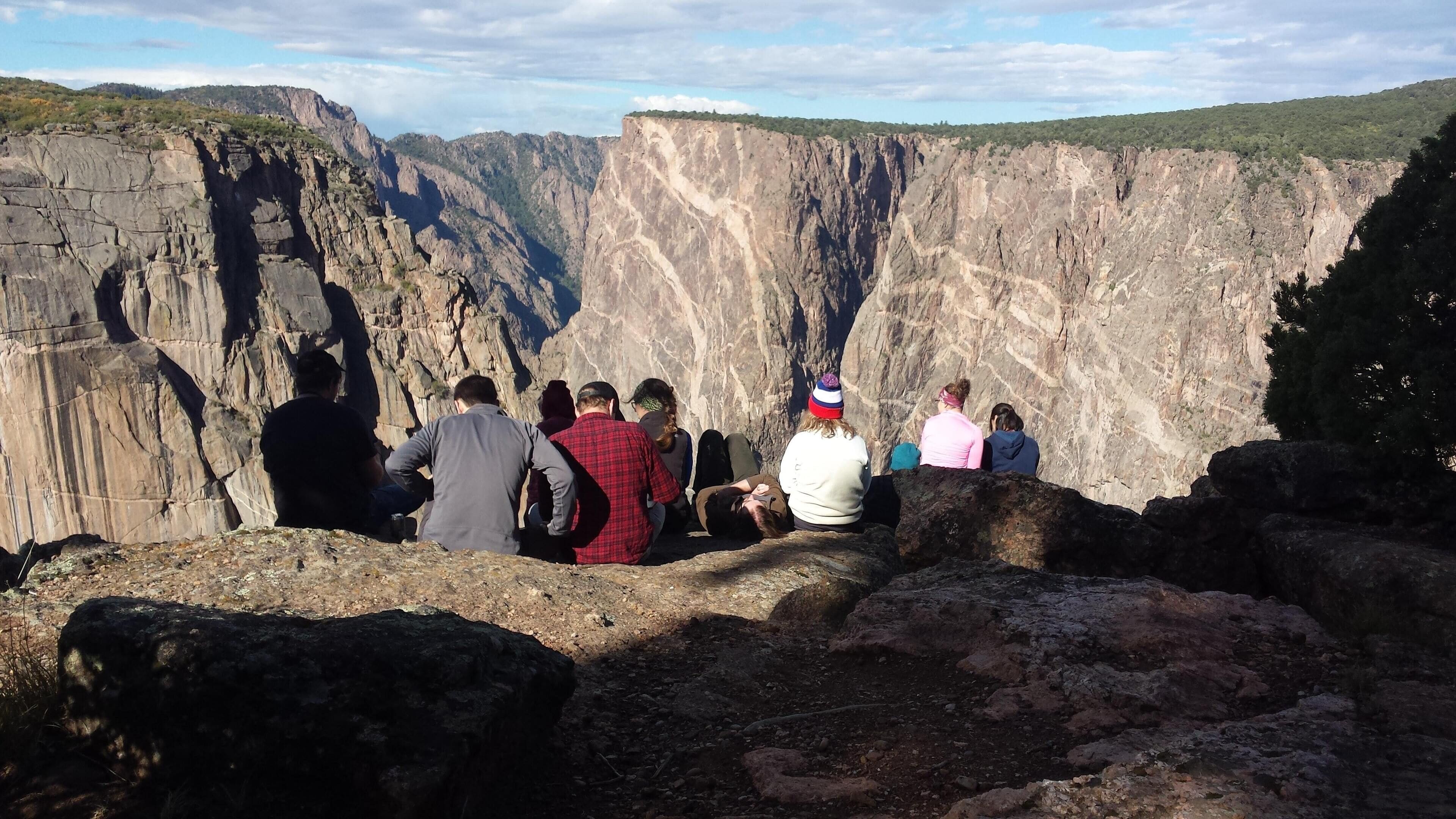 Een groep mensen zittend op rotsachtig terrein met uitzicht op een canyon.