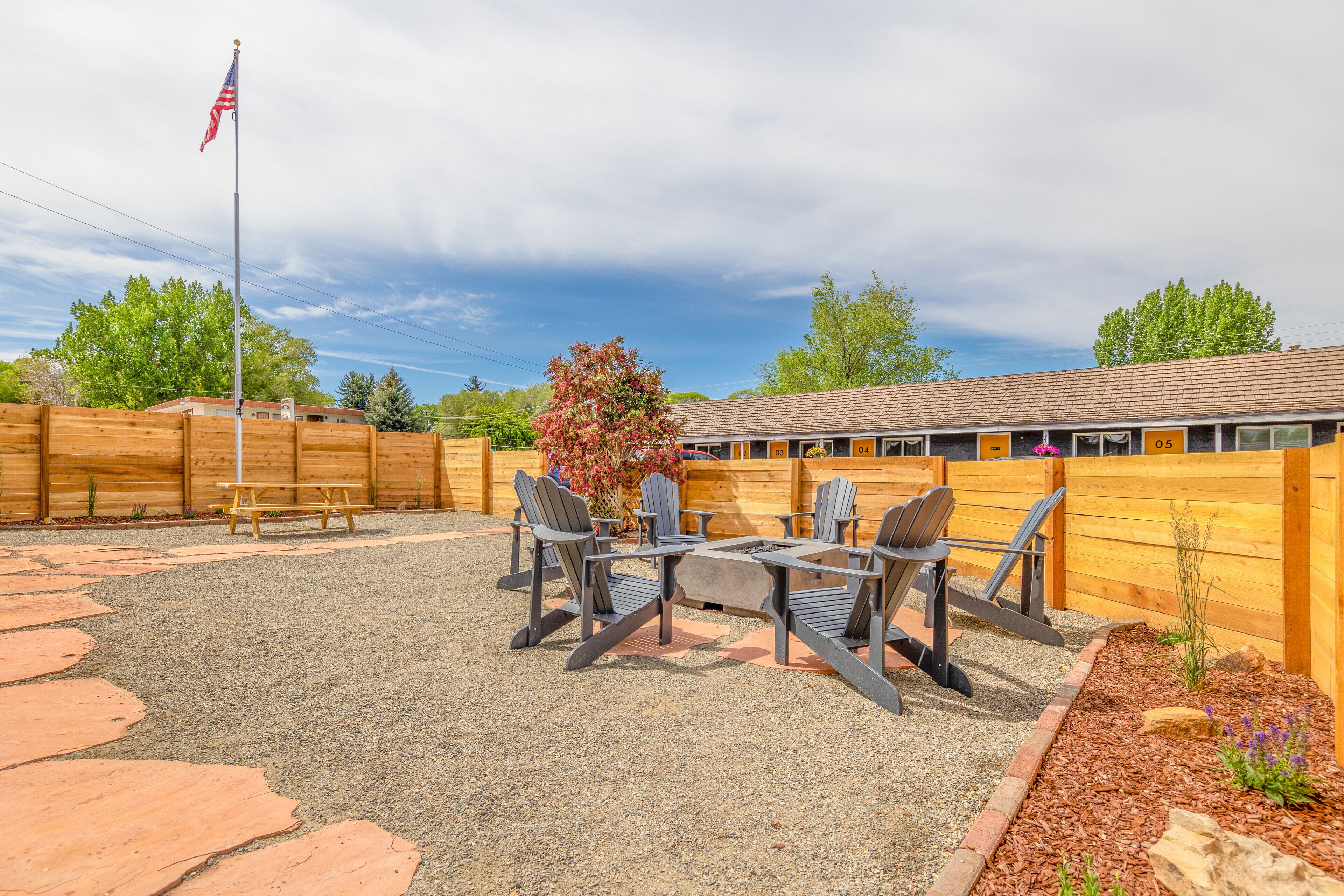 Une terrasse extérieure avec des fauteuils Adirondack, une table de pique-nique et un mât pour drapeau.