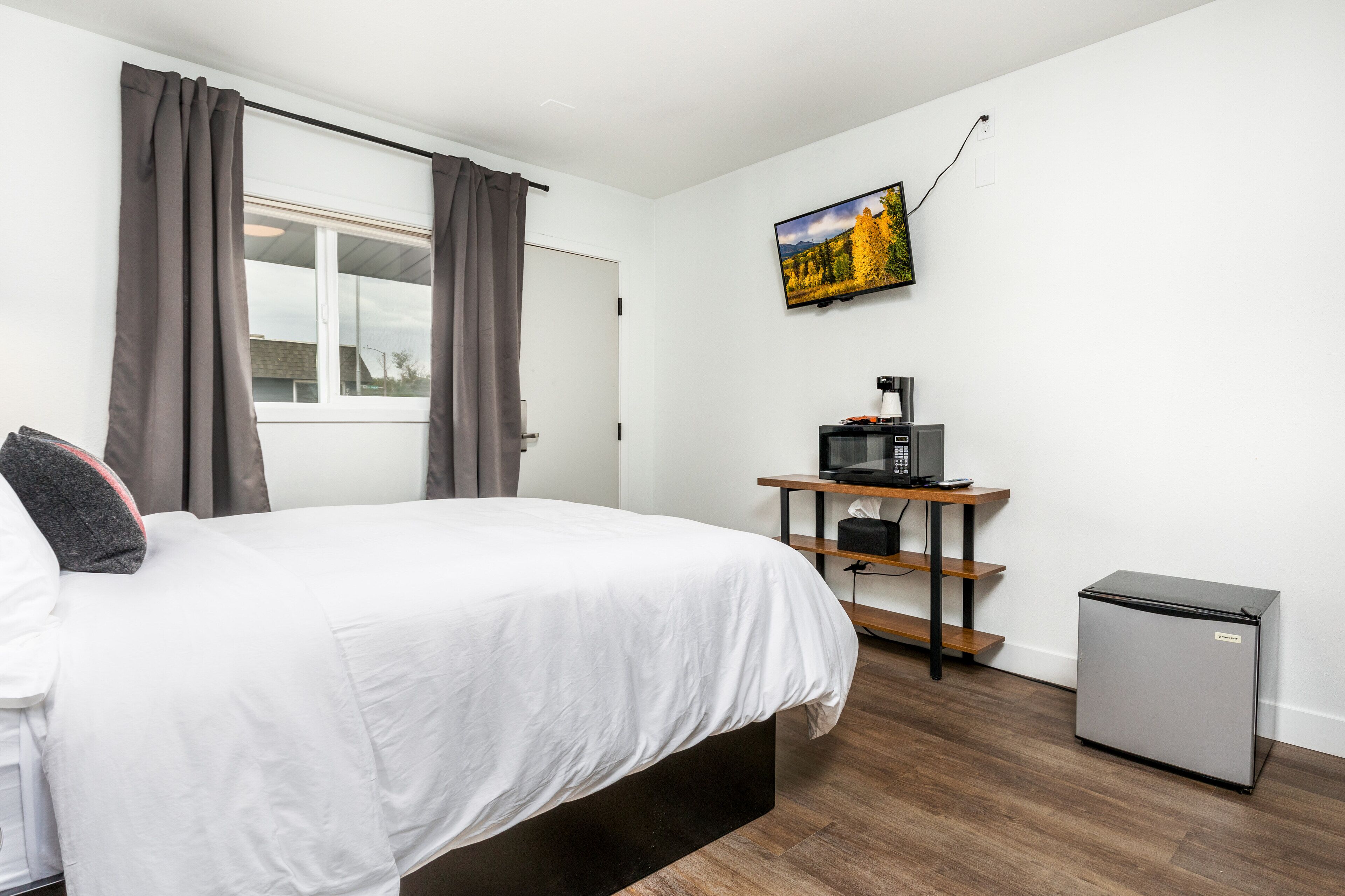 Una camera da letto con un letto, una scrivania con un computer, un frigorifero e una TV appesa al muro.