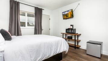 Una camera da letto con un letto, una scrivania con un computer, un frigorifero e una TV appesa al muro.