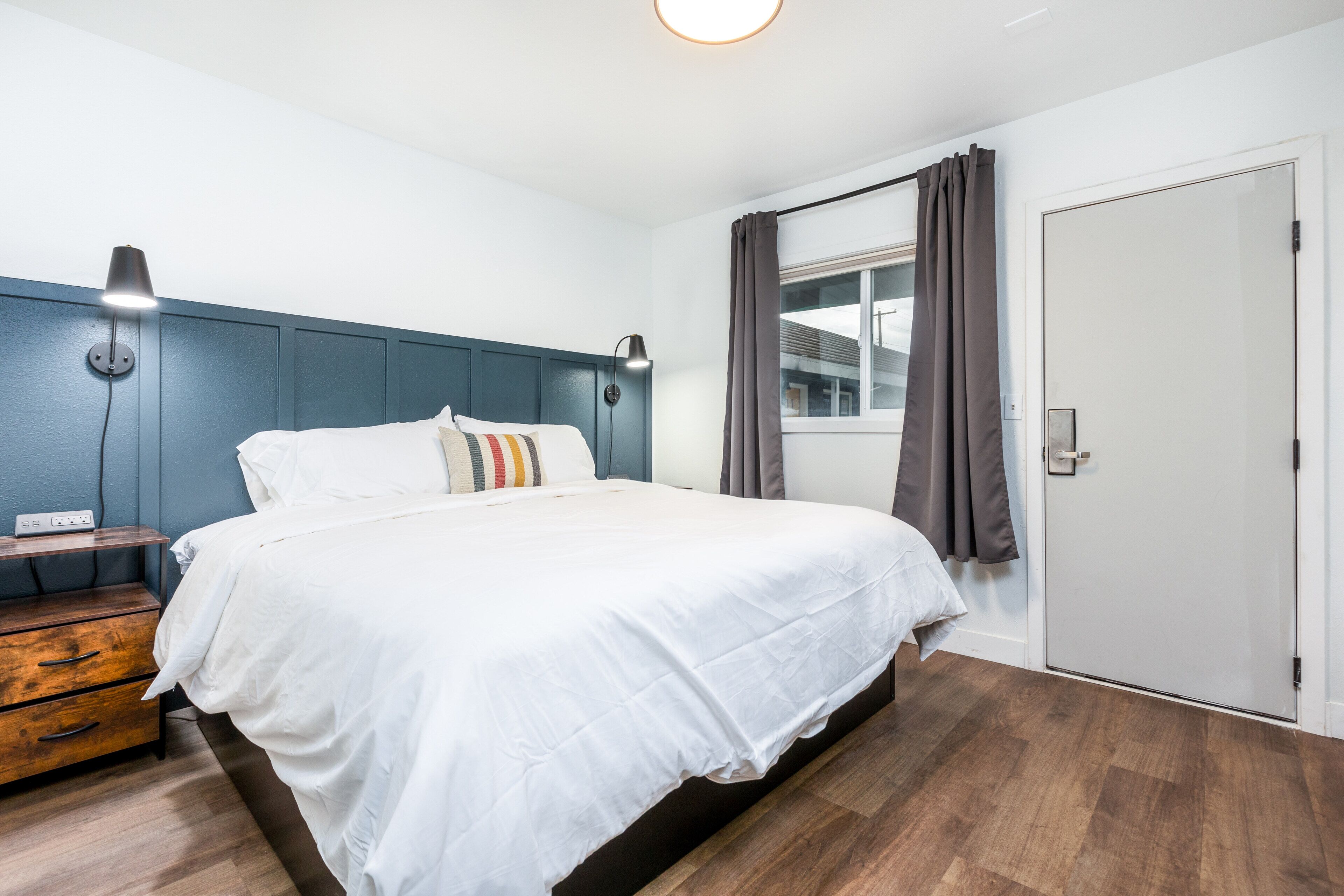 Een slaapkamer met een bed, nachtkastjes, een kledingkast, een raam met gordijnen en een wandlamp.