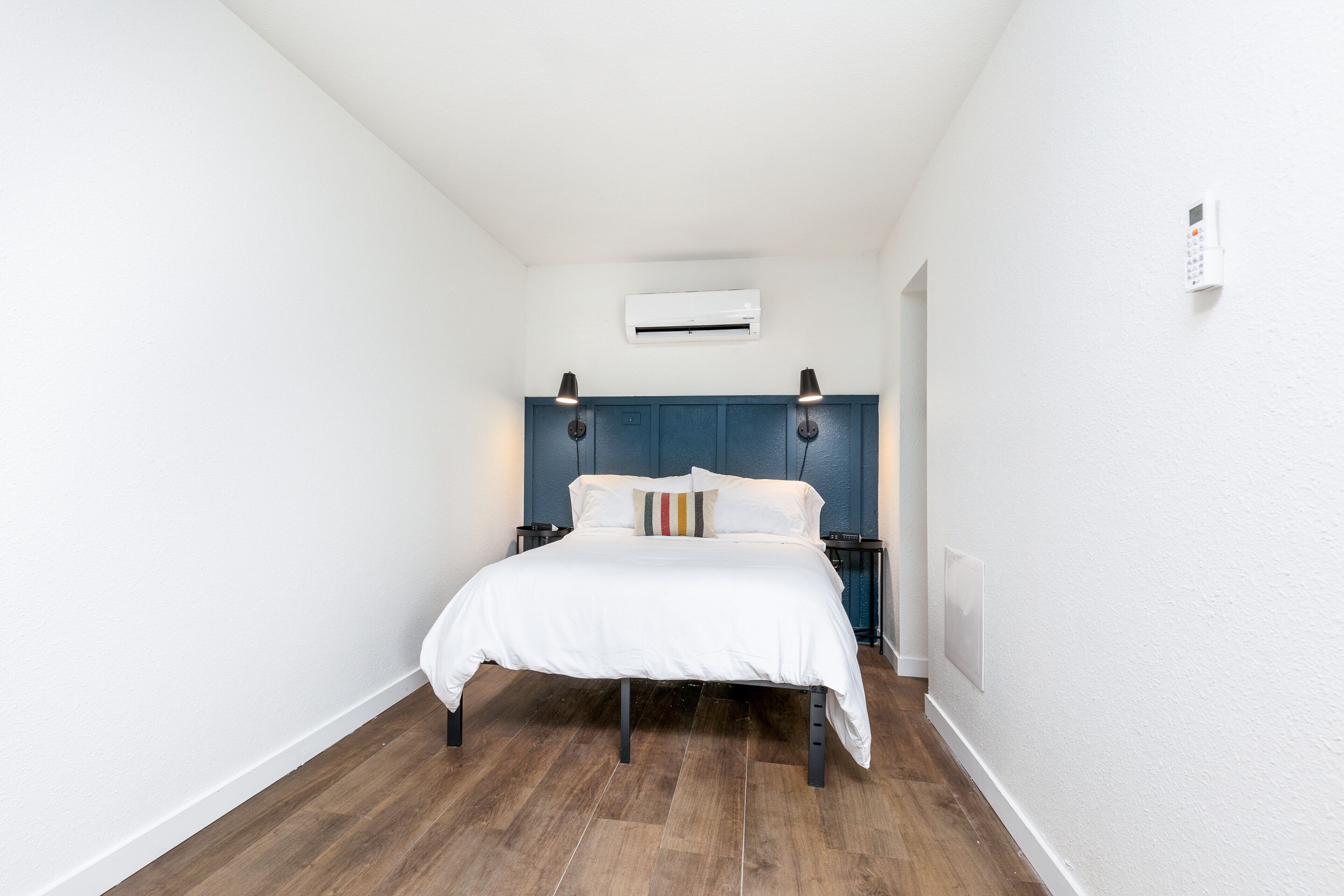 Un dormitorio con cama blanca, cabecero azul y suelo de madera.