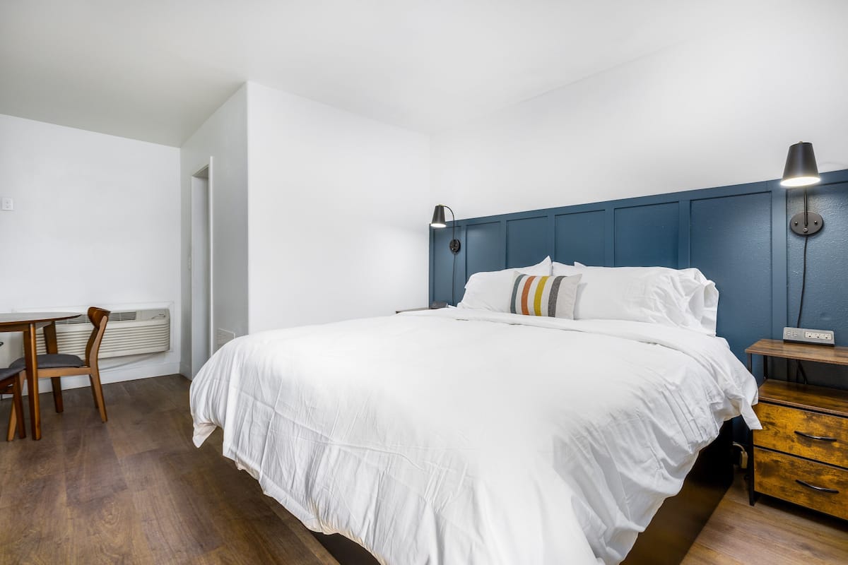 A bedroom with a bed, bedside table, lamp, and a chair.