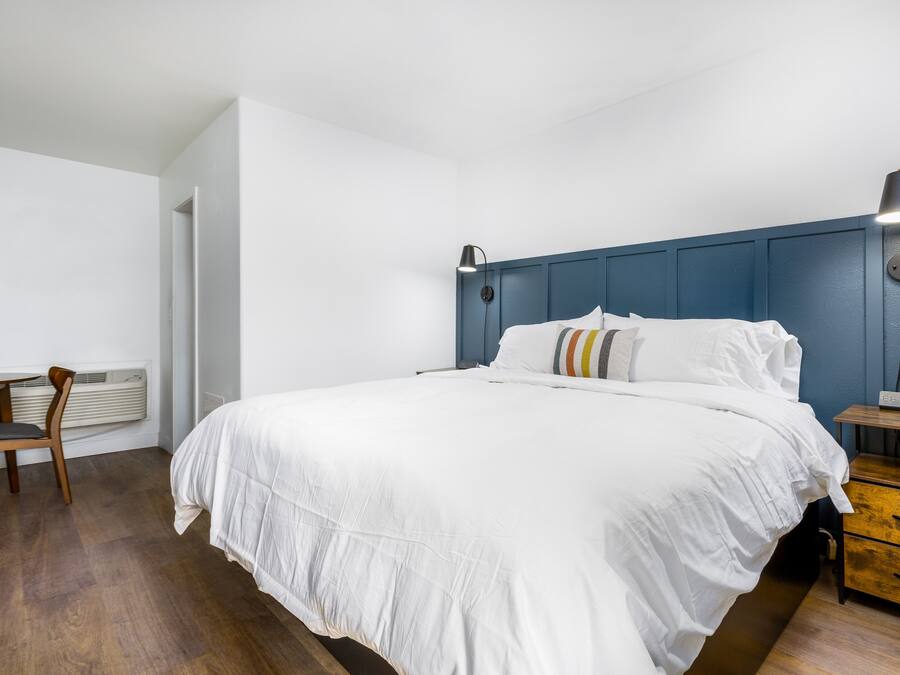 A bedroom with a bed, bedside table, lamp, and a chair.