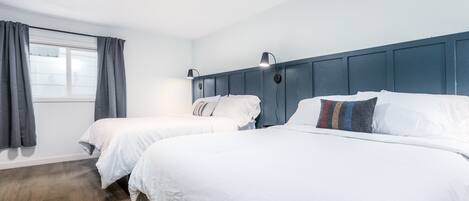 Une chambre d’hôtel avec deux lits, une fenêtre avec des rideaux, un plancher en bois et une tête de lit bleue.