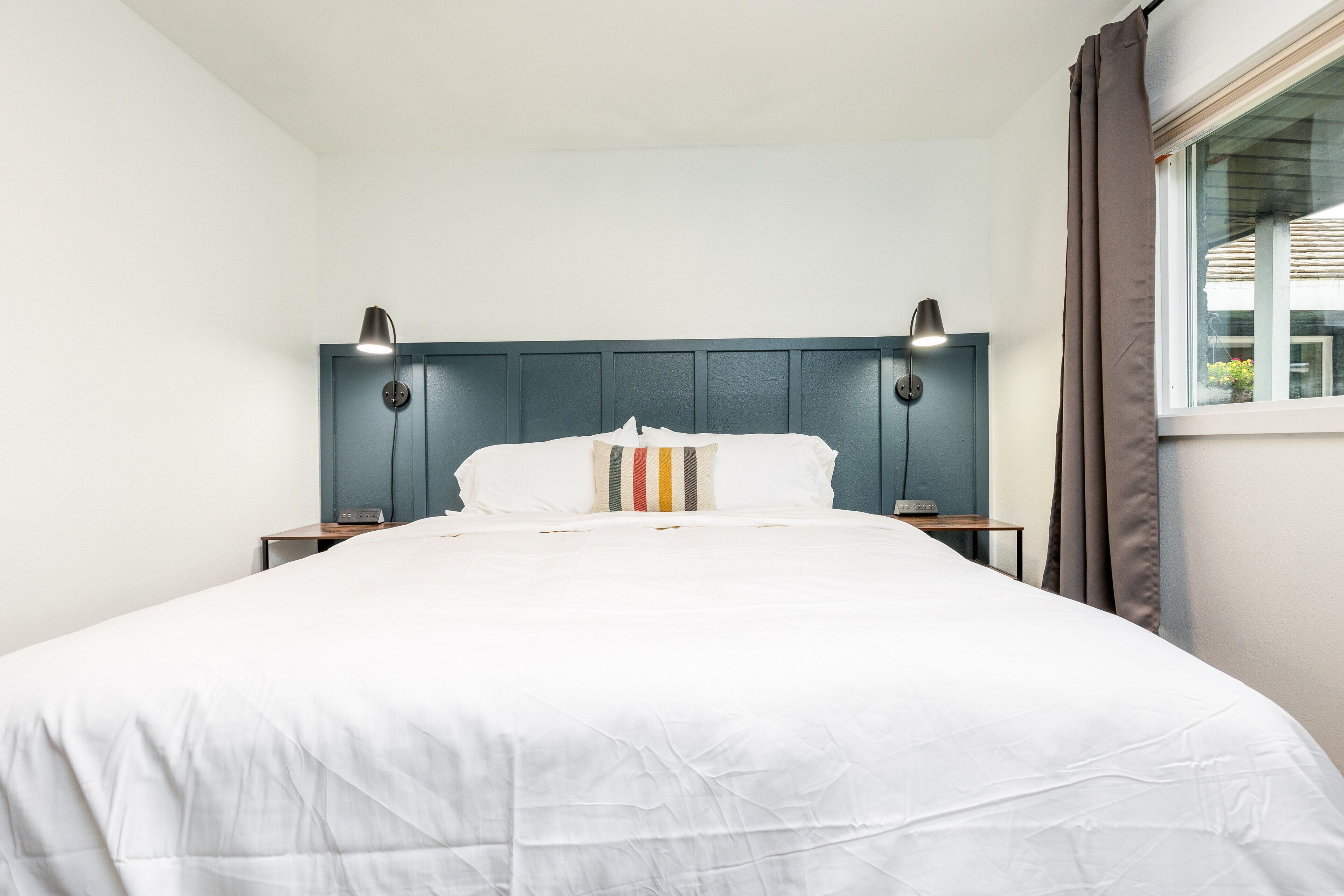 A neatly made bed with a white comforter and striped pillows, flanked by two bedside lamps on matching nightstands.