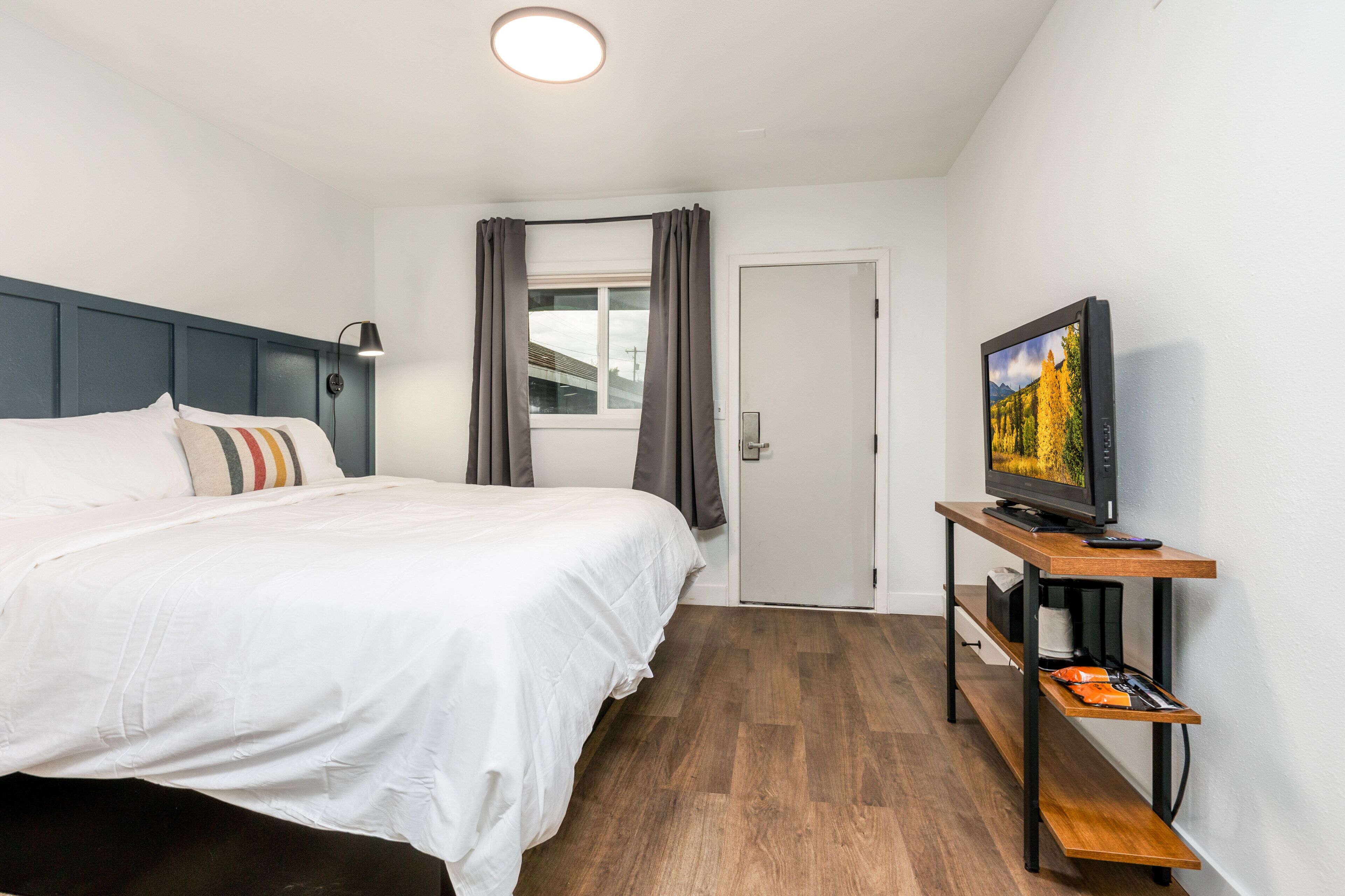 A hotel room with a bed, a television on a wooden stand, and a door leading to another room.