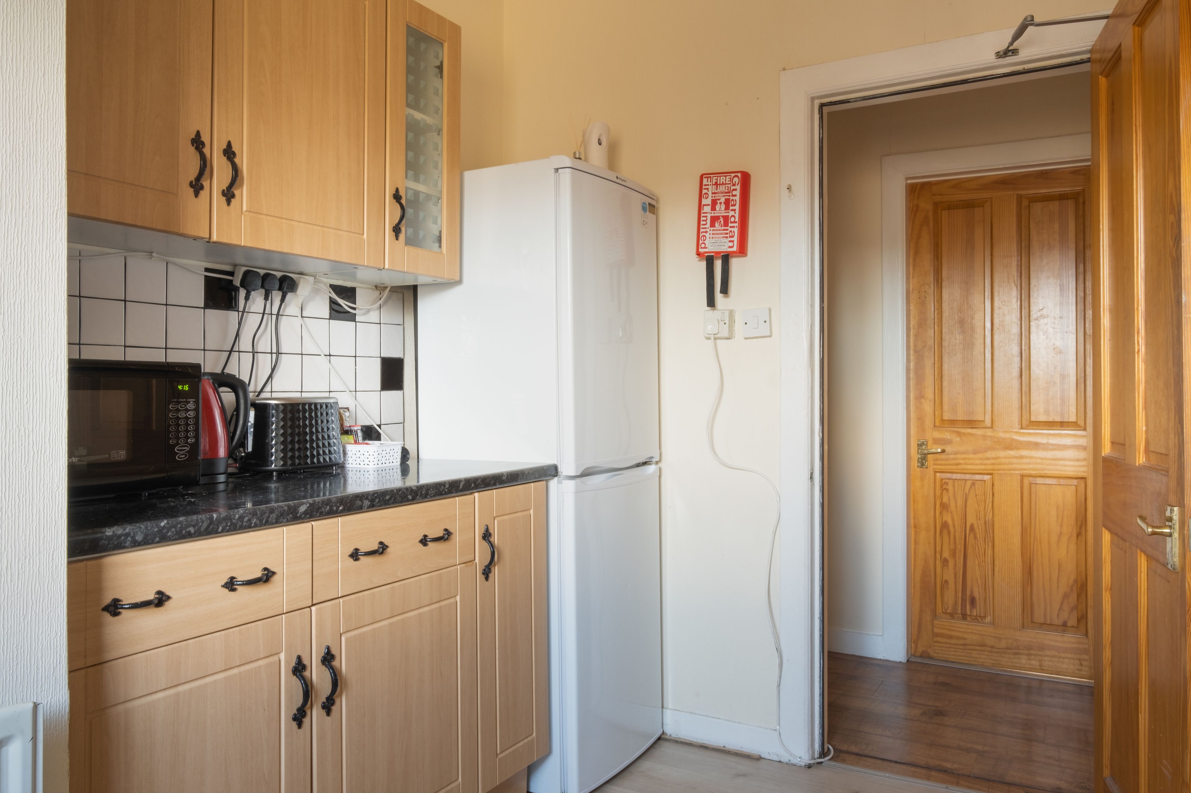 A kitchen with wooden cabinets, a white refrigerator, a microwave, and a kettle.