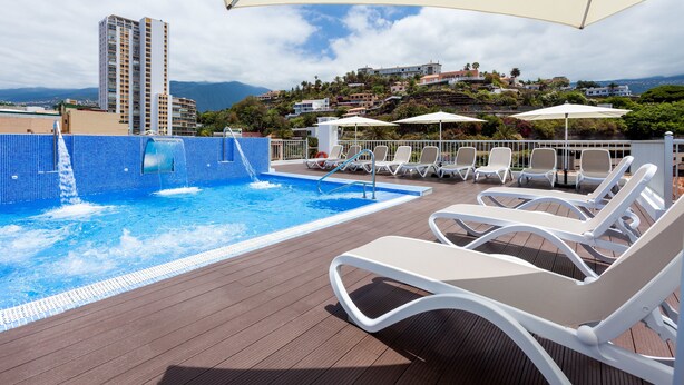 A rooftop pool area with lounge chairs and umbrellas, overlooking a cityscape with buildings and hills. - My City Hotel (Puerto de la Cruz)