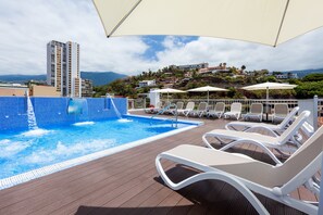 A rooftop pool area with lounge chairs and umbrellas, overlooking a cityscape with buildings and hills. - My City Hotel (Puerto de la Cruz)