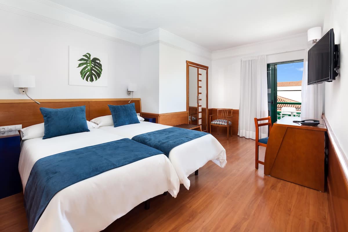 Camera d'albergo con due letti, una scrivania, una sedia, un televisore e vista all'esterno.