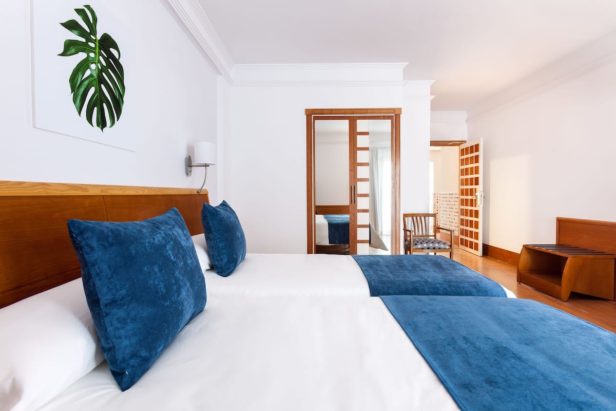 Camera d'albergo con un letto grande, due cuscini blu, una testata in legno, un comodino e una panca in legno.