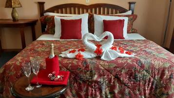 A hotel room with a floral bedspread, a bottle of champagne, two glasses, and a towel arranged in the shape of a swan.