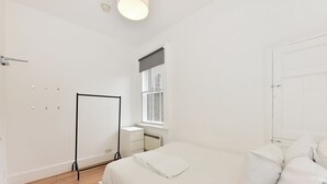 Un dormitorio con cama, mesita de noche, ventana con vistas, radiador y puerta.
