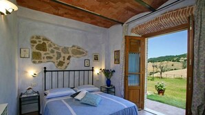 Une chambre à coucher avec un lit, un mur décoré de pierres, une porte en bois et une vue sur un paysage verdoyant.