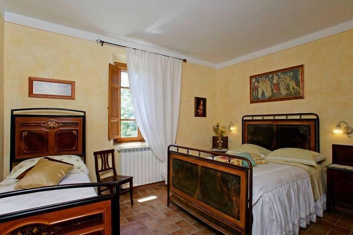 Une chambre avec deux lits, une fenêtre avec des rideaux, une chaise et un tableau au mur.