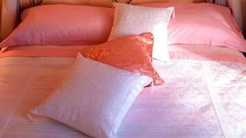 Una cama con cabecera de metal, ropa de cama rosa y blanca, y cortinas de gasa.