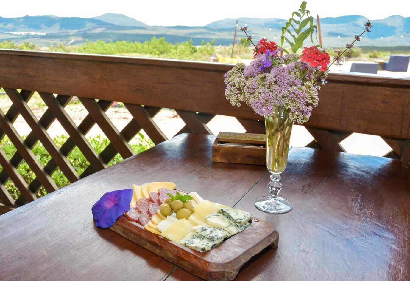 Une table en bois, une planche à fromage, un verre de vin et un vase de fleurs.