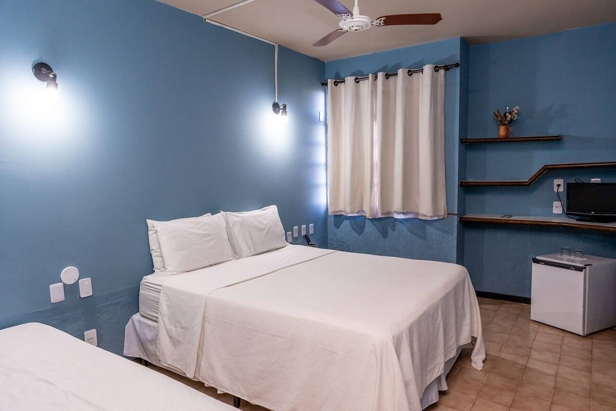 A hotel room with a bed, a small desk, a ceiling fan, a TV, and a mini-fridge.