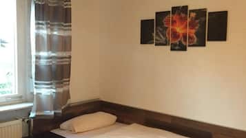 Une chambre à coucher comprenant un lit, une table de chevet, une fenêtre avec des rideaux et un mur orné de trois tableaux encadrés.