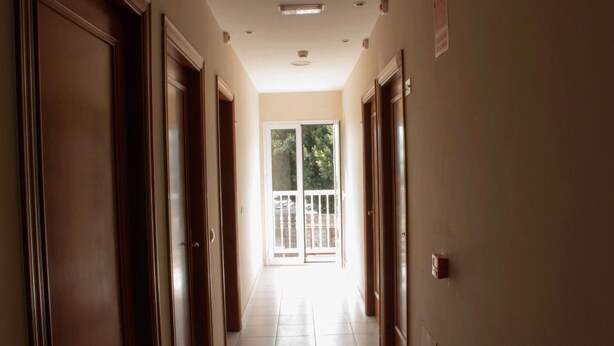Un couloir avec des portes en bois, un sol carrelé et une porte en verre donnant sur l’extérieur.