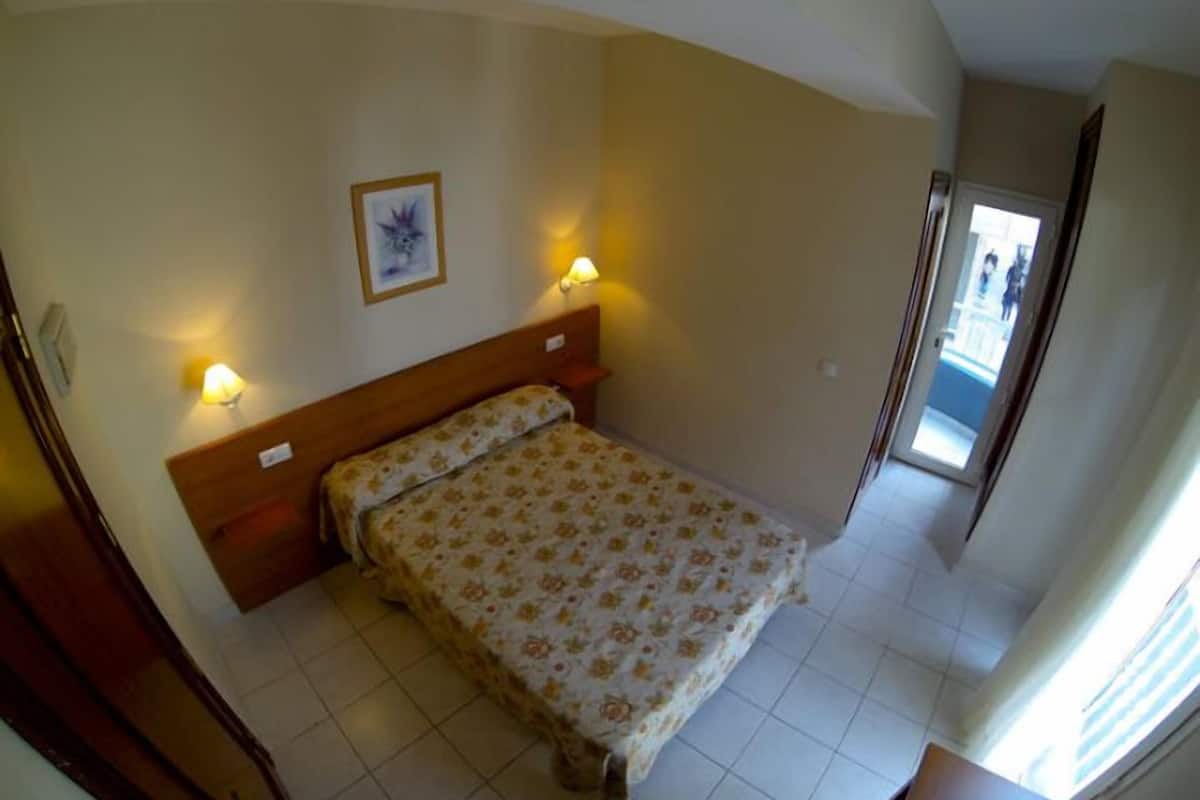 Une chambre à coucher avec un lit, deux lampes de chevet, un tableau encadré au mur et une porte donnant sur un balcon.