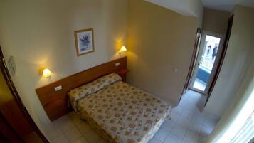A bedroom with a bed, two bedside lamps, a framed picture on the wall, and a door leading to a balcony.