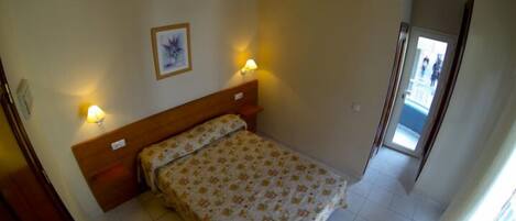 Un dormitorio con cama, dos lámparas de noche, un cuadro en la pared y una puerta que da a un balcón.