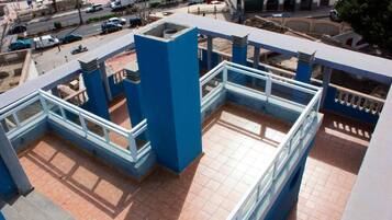 Una terrazza sul tetto con ringhiere blu e pavimento piastrellato, con vista su una strada con auto parcheggiate e palazzi.