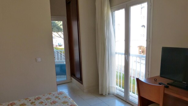Une chambre à coucher comprenant un lit, un bureau avec une chaise, un téléviseur et une porte-fenêtre coulissante donnant sur un balcon.