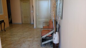 A hallway with a wooden door, a chair, and a decorative vase. - Hostal Virgen del Pilar (Baza)