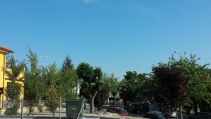 A parking lot with several cars, a yellow building, and trees. - Hostal Virgen del Pilar (Baza)
