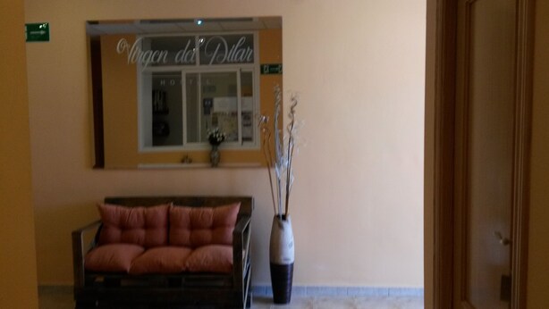 A reception area with a sofa, a vase with branches, and a sign above a window reading "Viren der Polder". - Hostal Virgen del Pilar (Baza)
