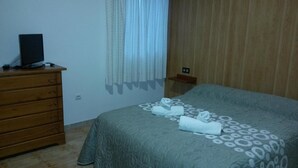 A bedroom with a bed, a wooden dresser, a television on the dresser, and a curtain. - Hostal Virgen del Pilar (Baza)