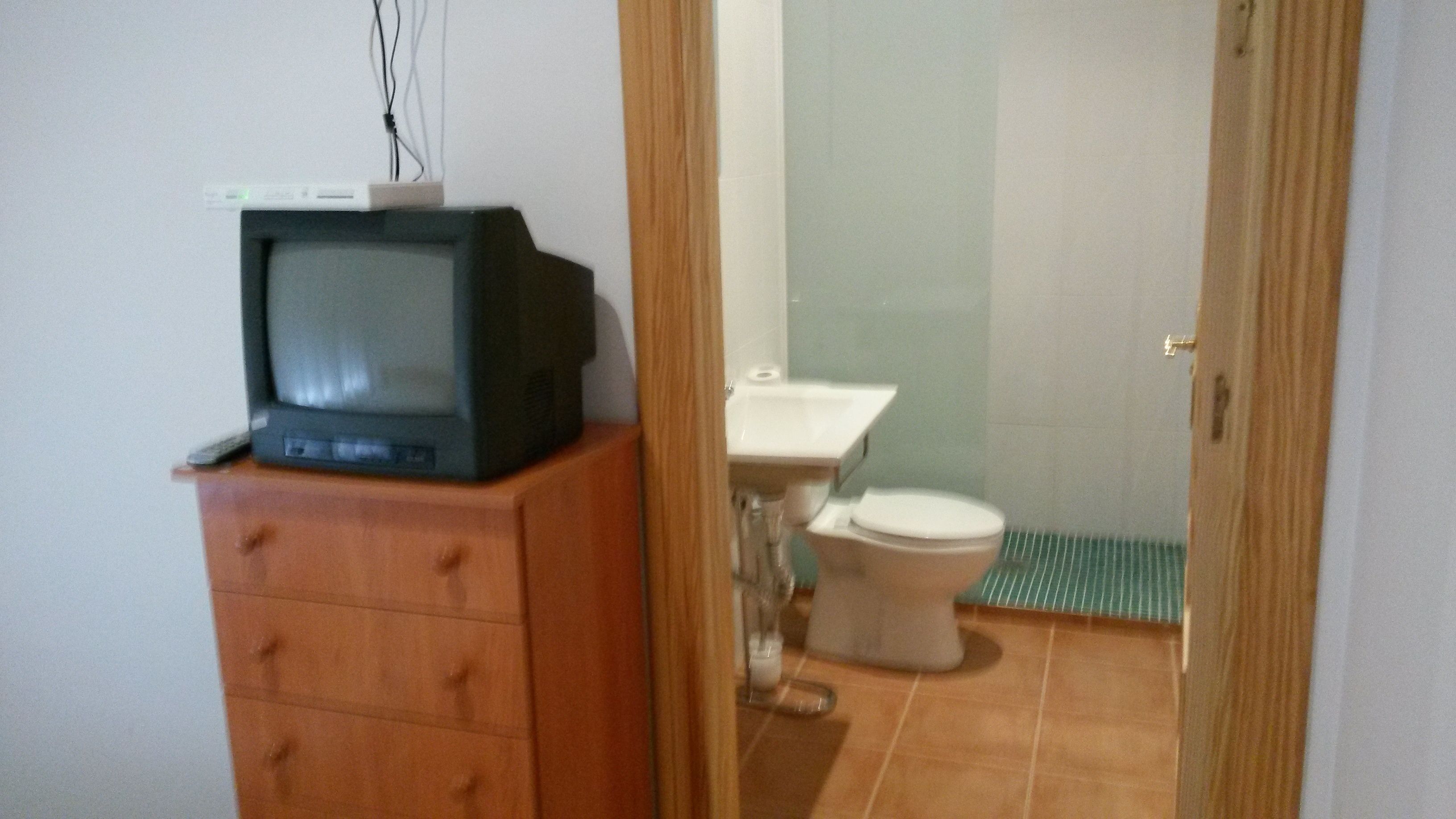 A small bathroom with a wooden cabinet, a toilet, and a television on top of the cabinet.