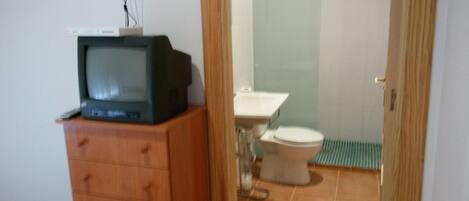 A small bathroom with a wooden cabinet, a toilet, and a television on top of the cabinet.