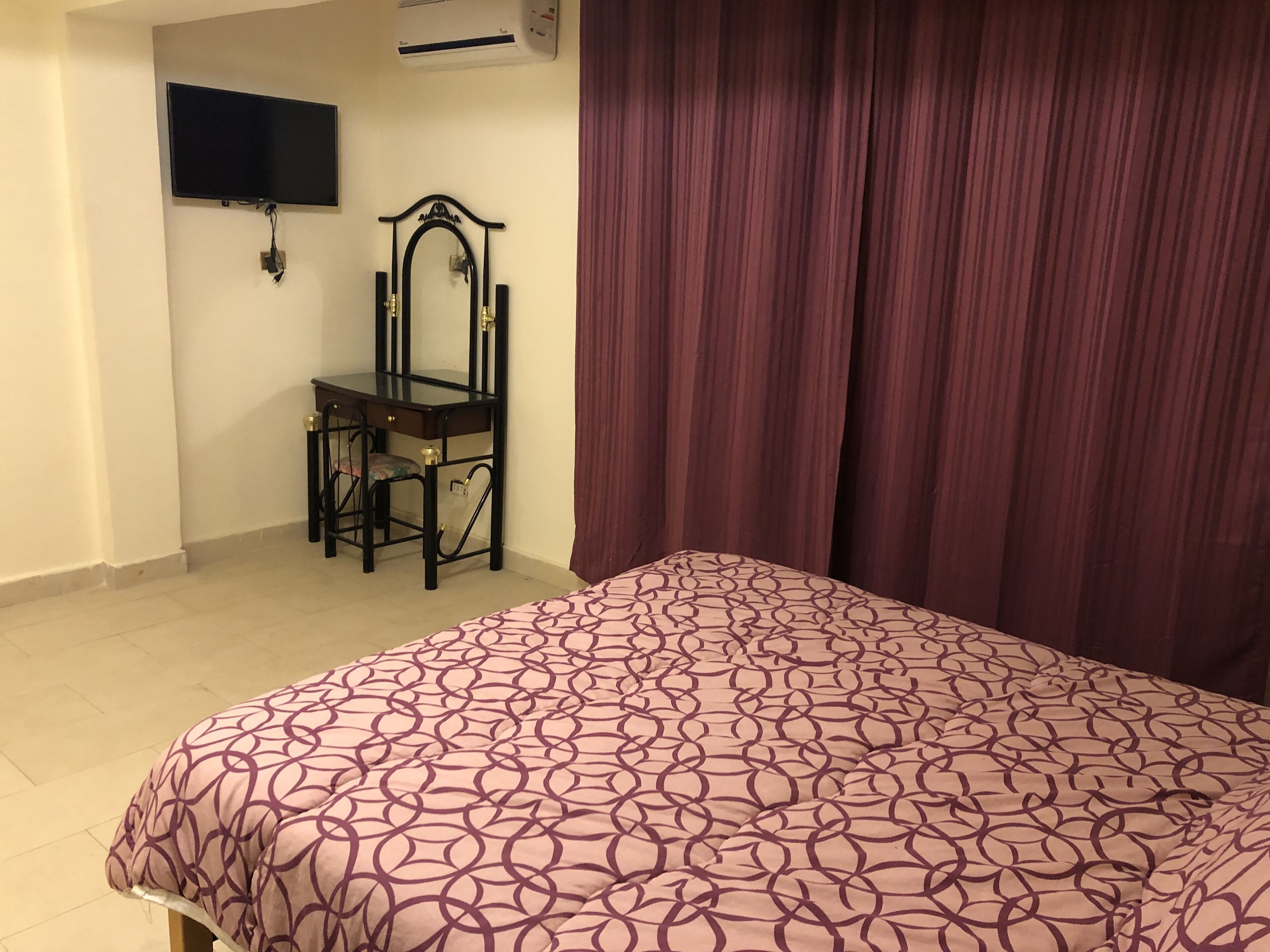 Un dormitorio con cama, escritorio, silla, televisor y cortina.