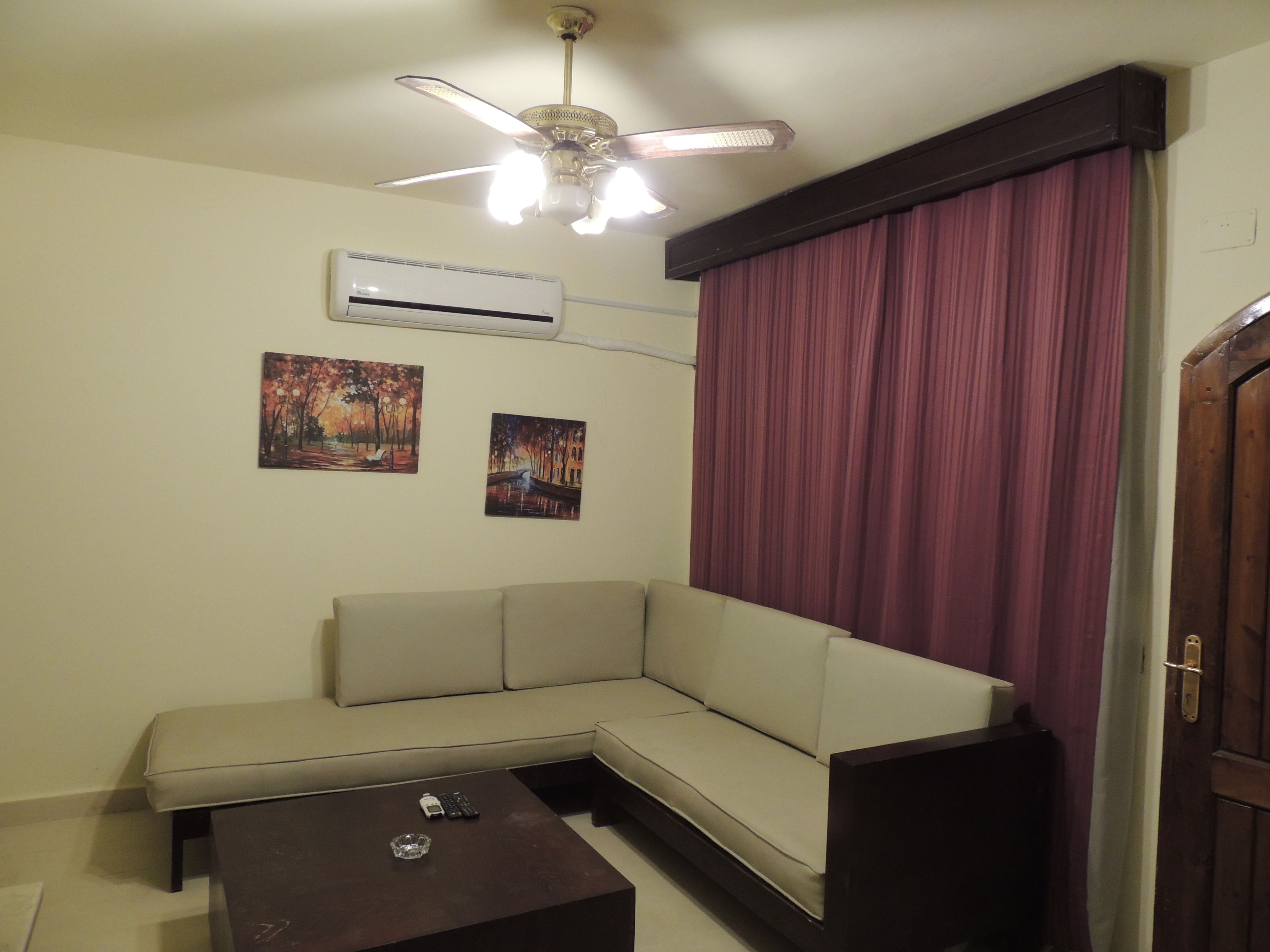 Uma sala de estar com um sofá bege, uma mesa de centro escura e duas pinturas na parede.