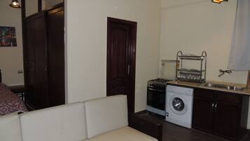 A compact living space with a sofa, a washing machine, a stove, and a sink.