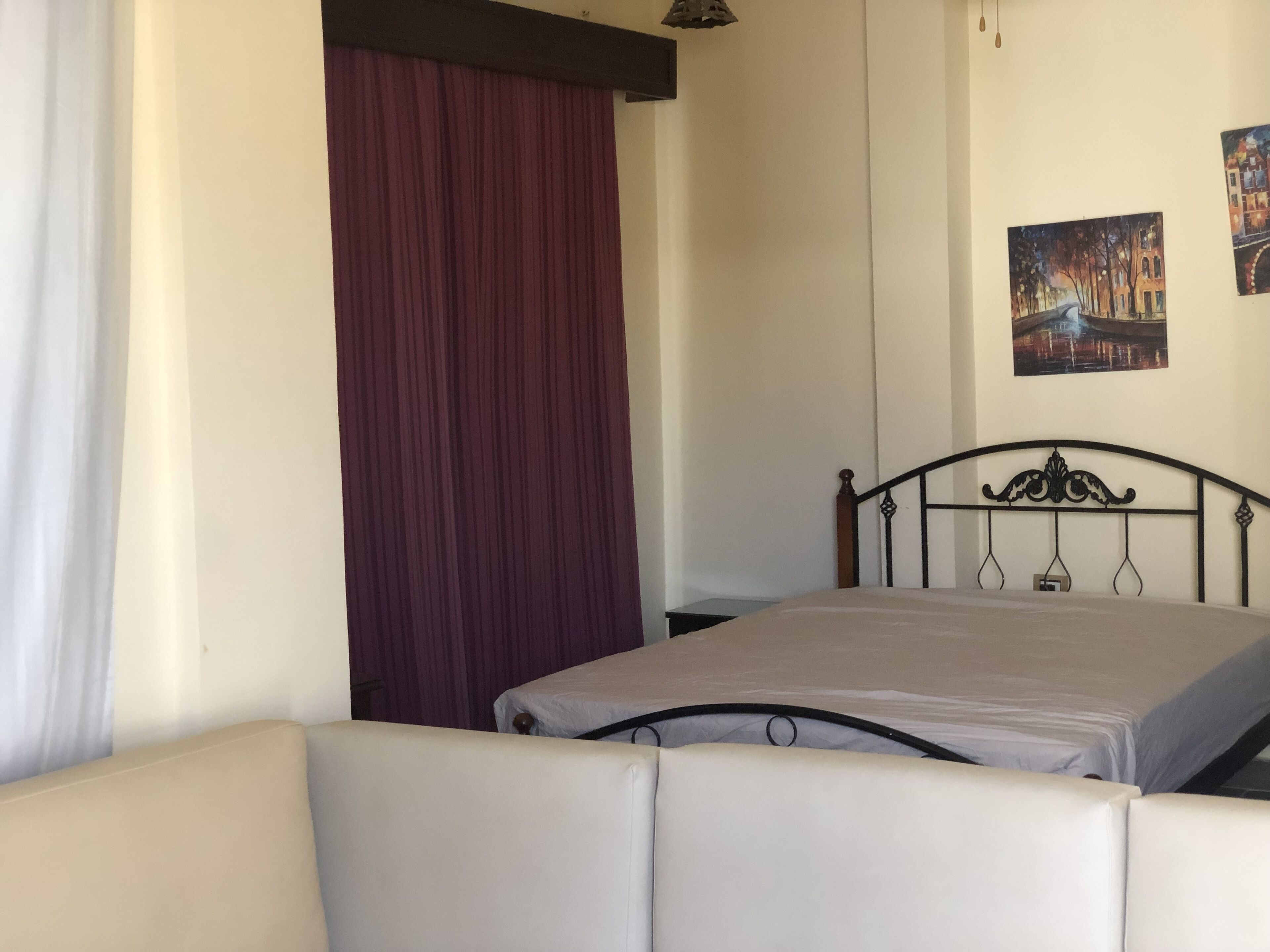 A room with a bed, a sofa, a curtain, and two paintings on the wall.