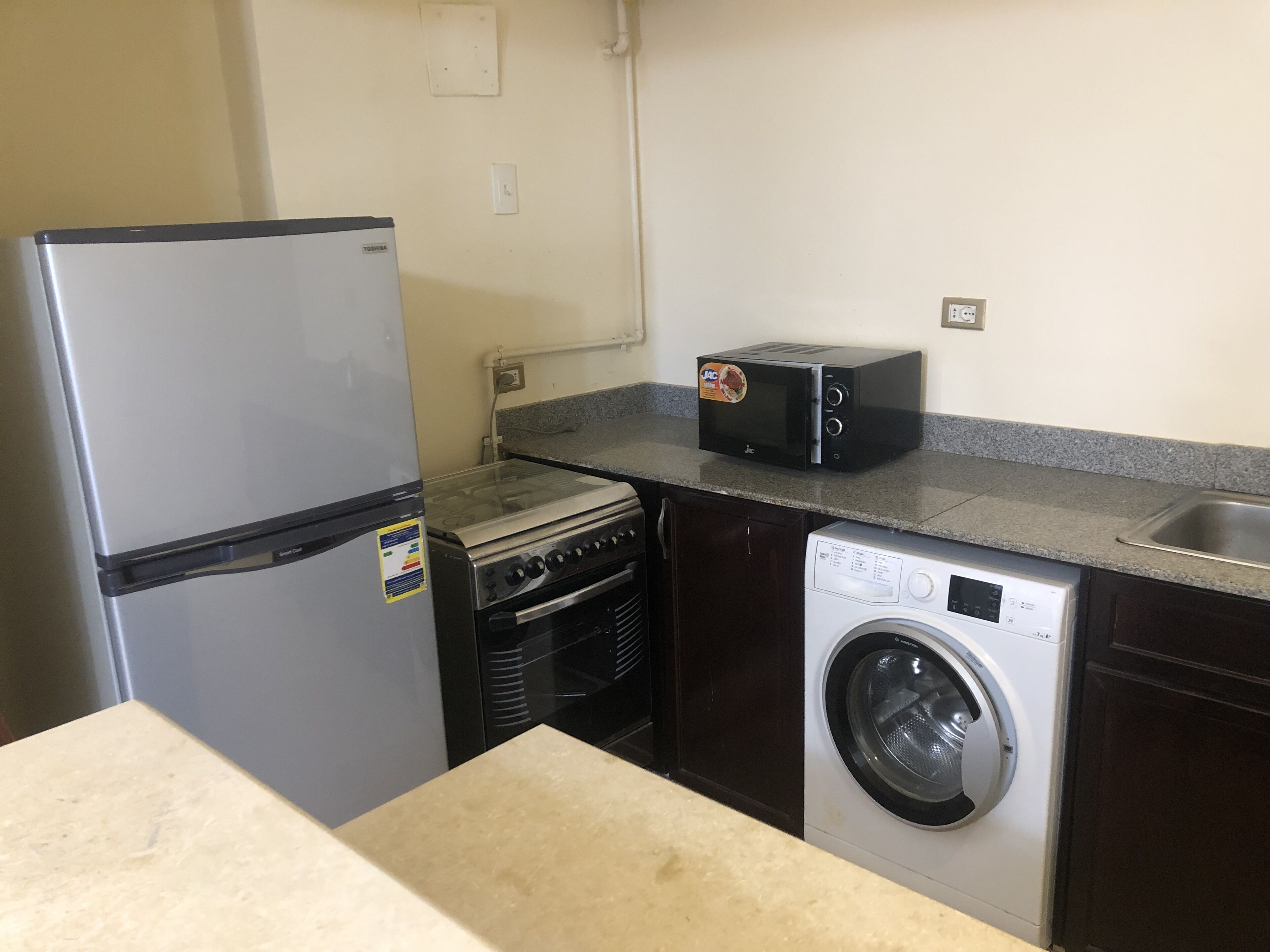 A compact kitchen with a refrigerator, microwave, stove, and washing machine.