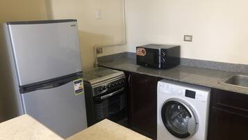 A compact kitchen with a refrigerator, microwave, stove, and washing machine.
