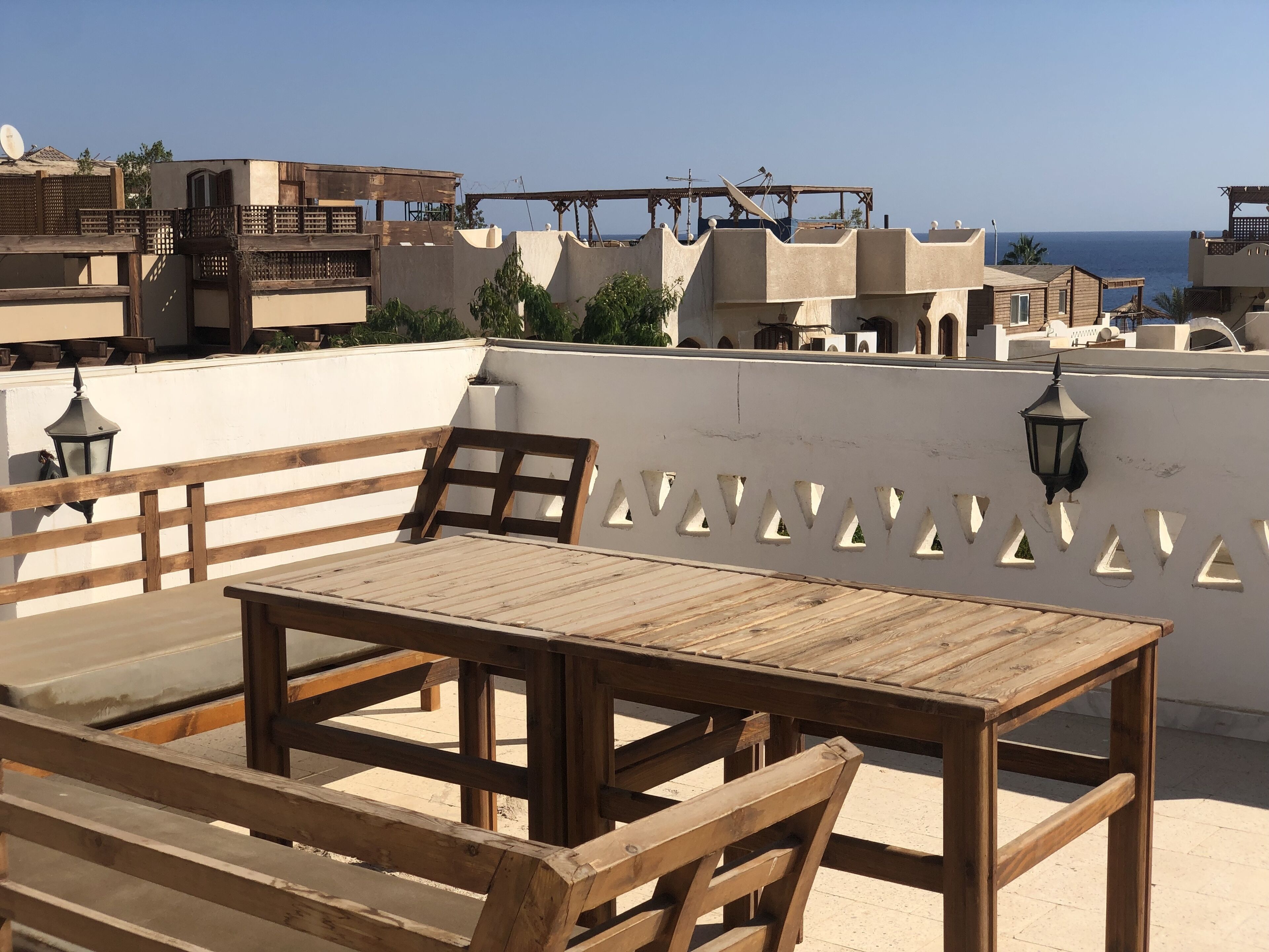 A wooden table and bench on a rooftop terrace with a view of the sea and buildings in the background.