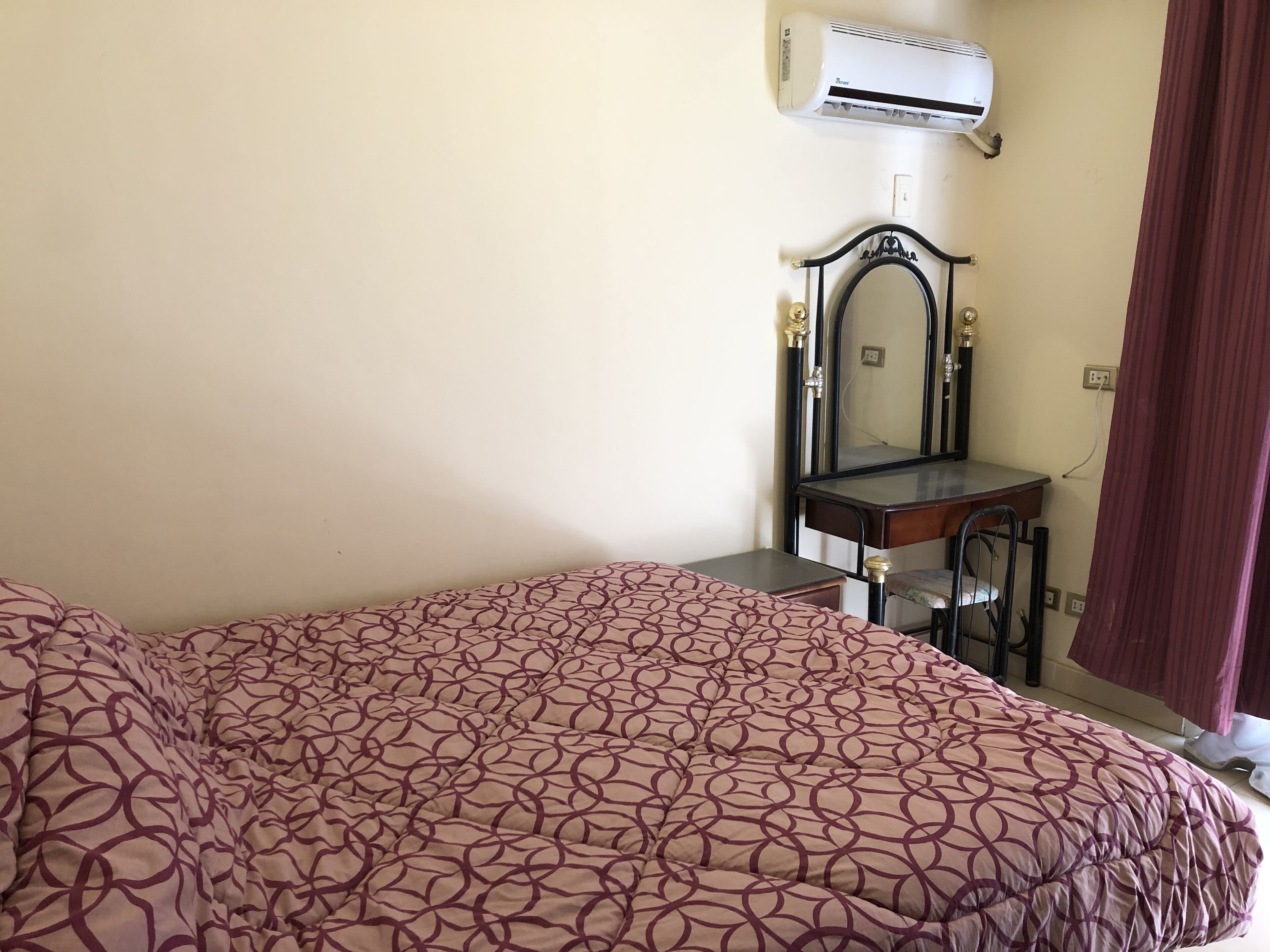 Quarto com cama, escrivaninha, cadeira, espelho e aparelho de ar condicionado.