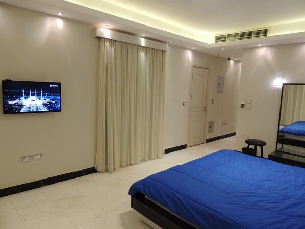 A hotel room with a large bed, a television mounted on the wall, a door, and a mirror. - Sultan Dusit Villa New Cairo (New Cairo)
