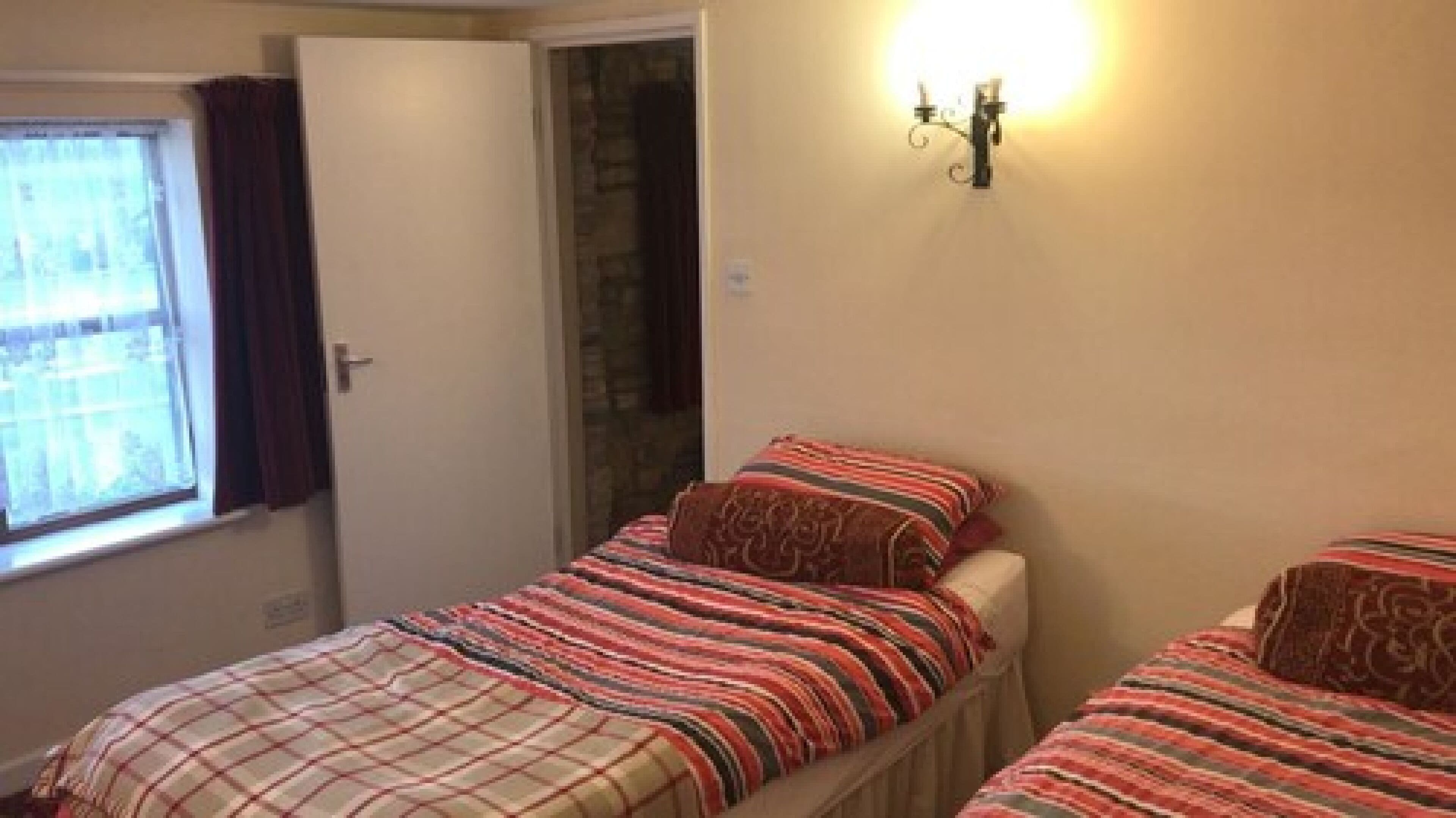 Una camera da letto con due letti, una finestra con tende e un lampadario a parete.