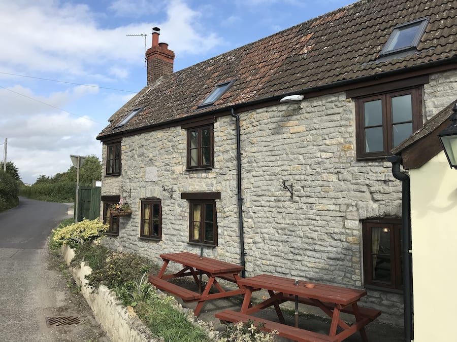A stone building with a tiled roof, multiple windows, and a picnic table outside.