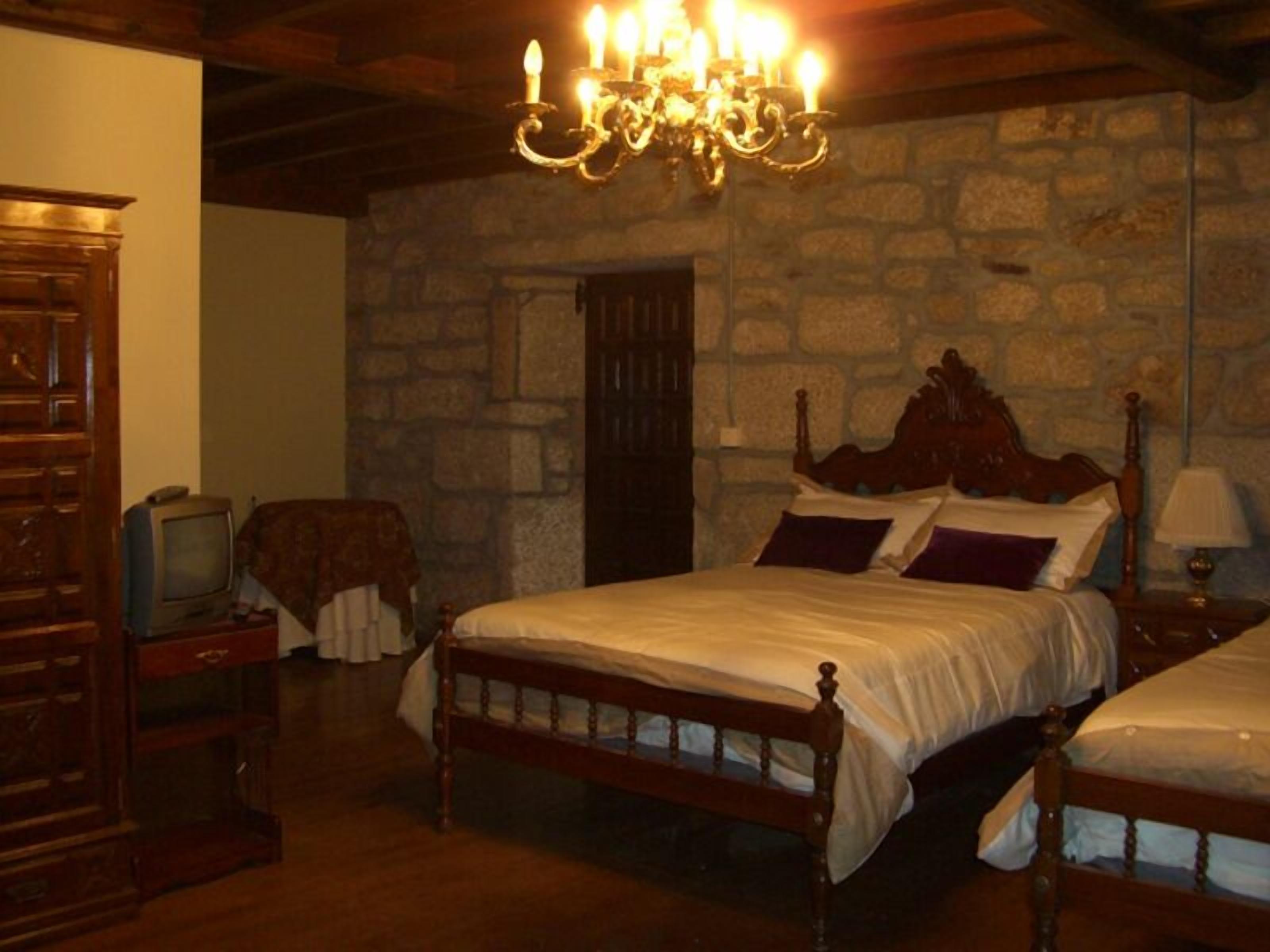 A traditional room with a stone wall, a wooden bed with a headboard, a television, and a chandelier.